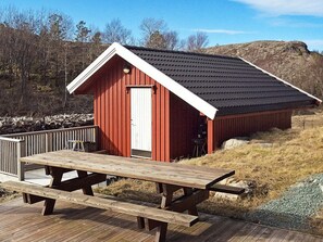 A red wooden cabin with a white door and a black roof, situated on a wooden deck with a picnic table in front. - 4 Star Holiday Home in Oksvoll (Orland)