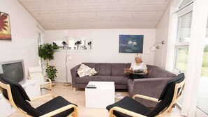 A modern living room with a grey sofa, two black and wooden armchairs, a white coffee table, a floor lamp, a TV, and a large window. - 9 Person Holiday Home in Brovst (Brovst)