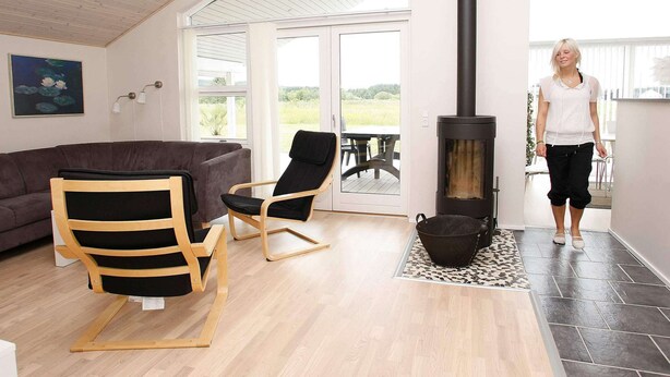 A cozy living room with a sofa, two chairs, a fireplace, and a large window offering a view of the outdoors. - 9 Person Holiday Home in Brovst (Brovst)
