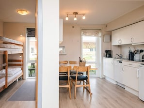 A modern kitchen with white cabinets, a dining area with wooden chairs, and a bunk bed with a light fixture. - 6 Person Holiday Home in Romo (Rømø)