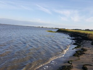A coastal landscape with a sandy beach, calm water, and distant buildings. - 6 Person Holiday Home in Romo (Rømø)
