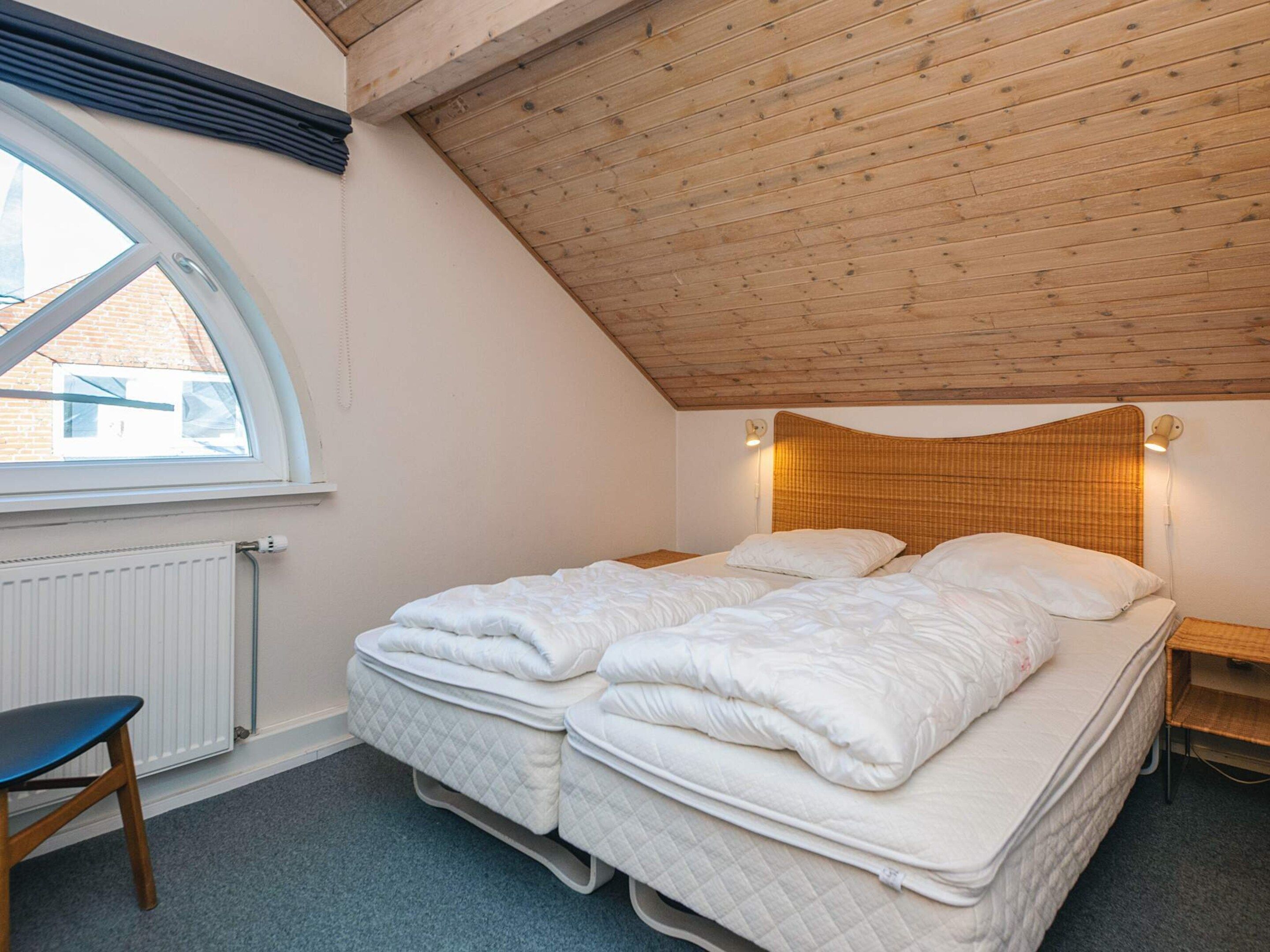 Une chambre avec un plafond en pente, un lit avec deux oreillers, une table de chevet et une chaise.
