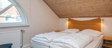 Une chambre avec un plafond en pente, un lit avec deux oreillers, une table de chevet et une chaise.