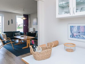 A modern living room with a sofa, chairs, a dining table, and a kitchen area with cabinets.