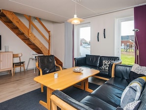 A modern living room with a wooden staircase, a black leather sofa, a wooden coffee table, and a view of the outdoors. - 6 Person Holiday Home in Romo (Rømø)