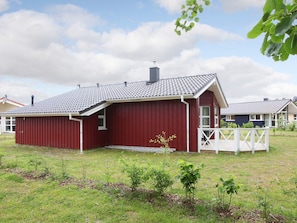 A red building with a sloped roof, a white fence, and a grassy yard with young plants. - Holiday Home in GrÃ¶mmitz (Groemitz)