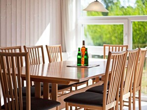 A dining table with six wooden chairs, a pendant light, and two bottles on a coaster. - Holiday Home in GrÃ¶mmitz (Groemitz)