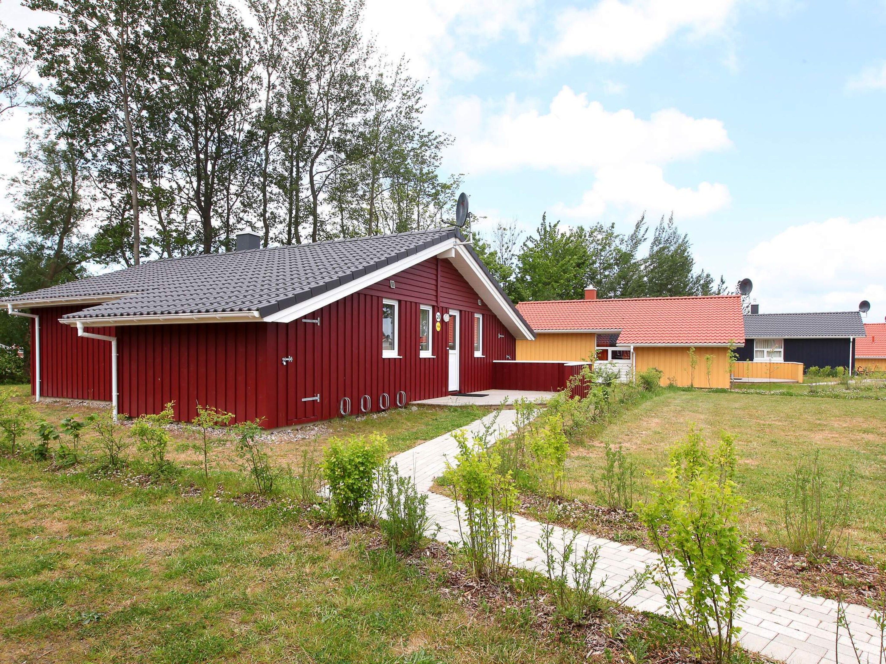 Un bâtiment rouge avec un toit en tuiles, un chemin pavé et une zone herbeuse avec de jeunes arbres.