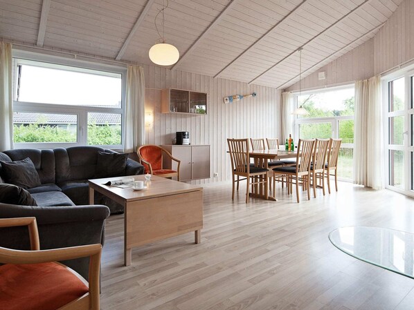 Una sala de estar moderna con sofá, mesa de centro y zona de comedor con sillas y una mesa de vidrio.