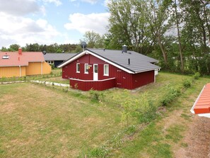 A red single-story house with a grey roof, surrounded by a grassy yard and trees. - Holiday Home in GrÃ¶mmitz (Groemitz)