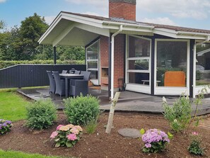 A covered patio area with a table and chairs, surrounded by flower beds and a brick wall.