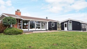 Une maison moderne à deux étages, dotée d’une grande pelouse à l’avant, d’une véranda et d’un garage séparé.