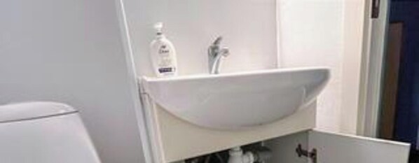 A bathroom with a white sink, a mirror, and a bottle of hand soap.