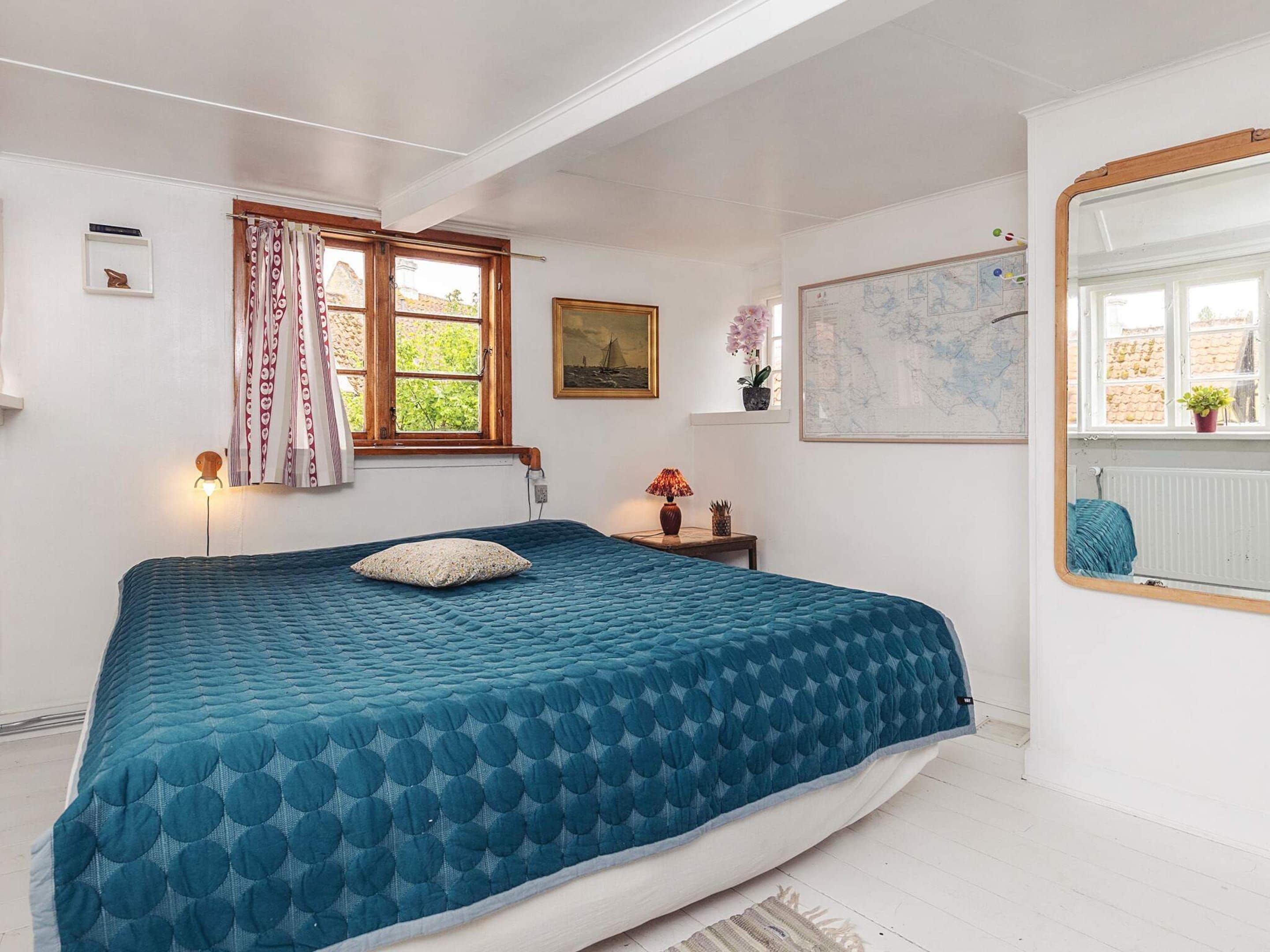 A bedroom with a bed, a window with curtains, a map on the wall, and a mirror.