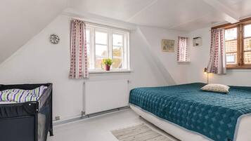 Een slaapkamer met een bed, een radiator, een raam met gordijnen en een kleine plant.