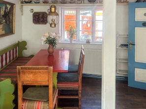 A dining area with a red table, wooden chairs, and a bench. There is a window with a view of the street, and a door to the right. - 4 Person Holiday Home in Aeroskobing (Aeroskobing)