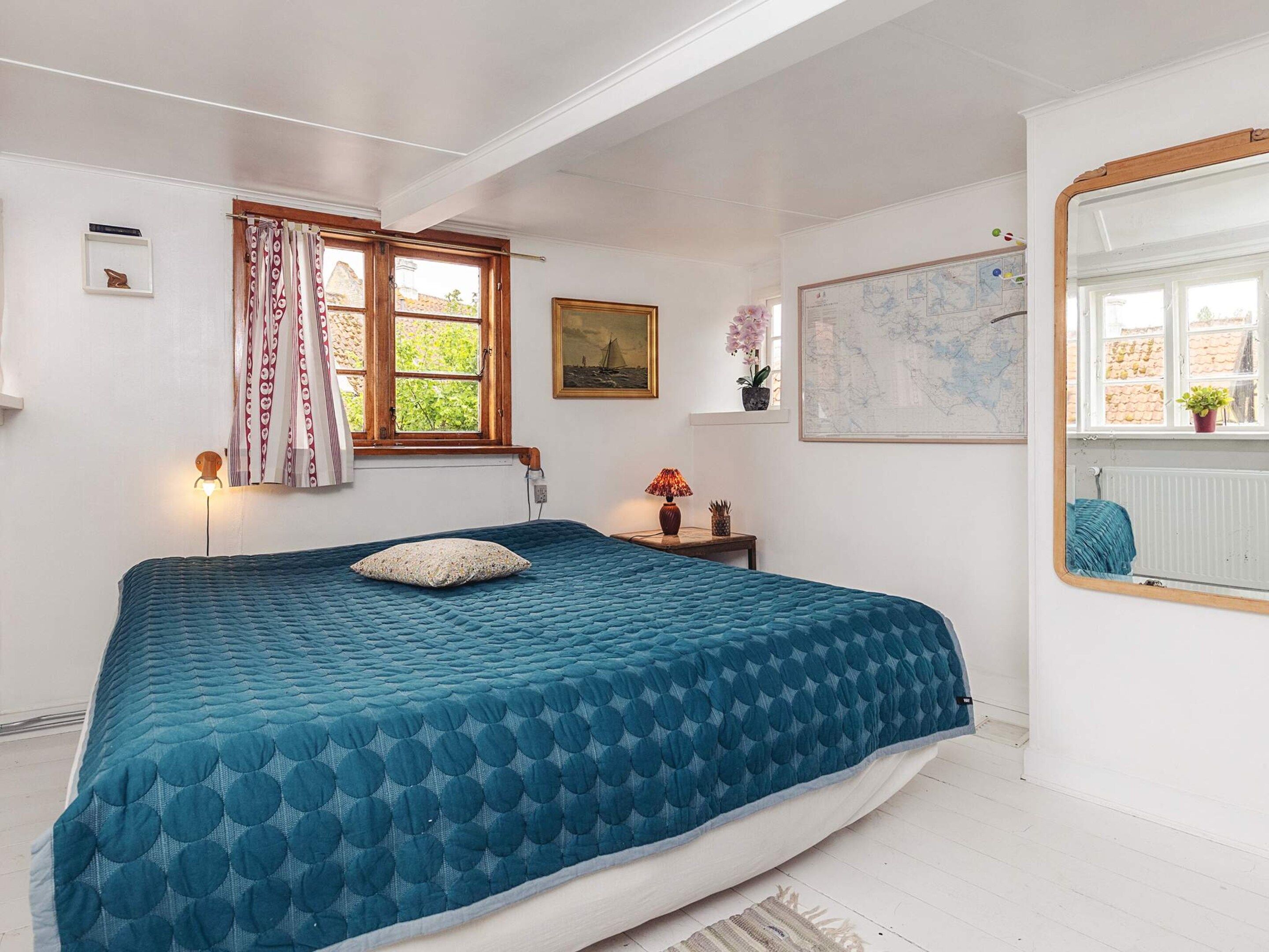 A bedroom with a bed, a window with curtains, a map on the wall, and a mirror.