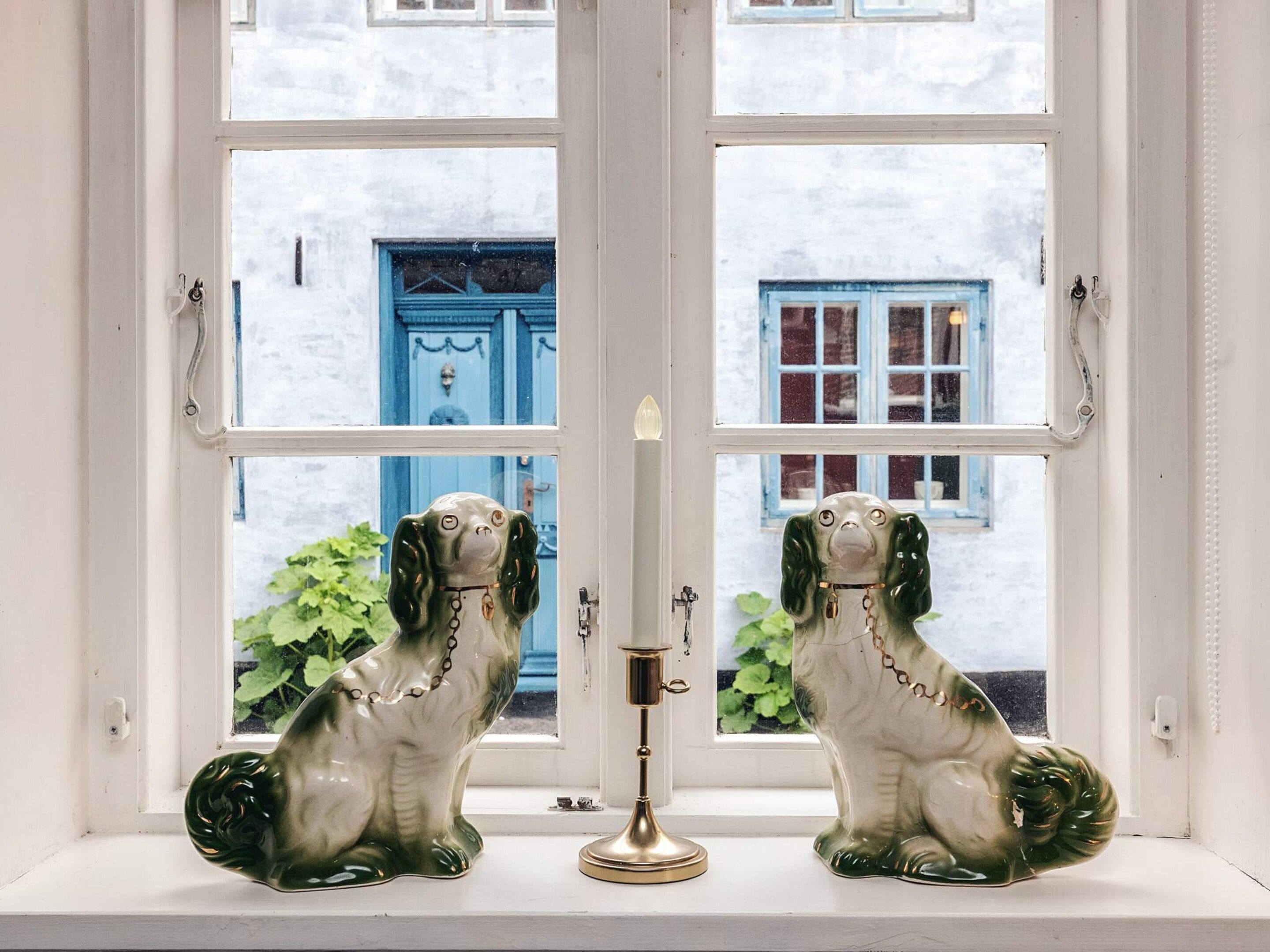 Two ceramic dog figurines on a windowsill, with a brass candlestick between them.