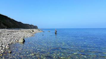 A rocky beach with clear water, a person standing in the water, and a cliff in the background.