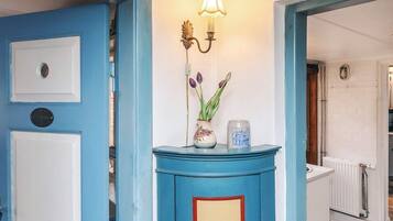 Una puerta azul con un picaporte blanco, una lámpara fijada a la pared y un jarrón con flores.