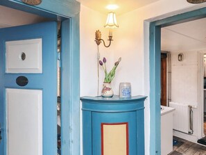 Une porte bleue avec une poignée blanche, un luminaire fixé au mur et un vase rempli de fleurs.