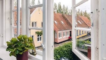 Una ventana con una planta en maceta, vista a un barrio residencial con casas y una estación de tren.