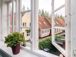 Et vindue med en potteplante, udsigt til et boligområde med huse og en togstation.