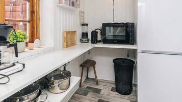 A compact kitchen with a microwave, coffee maker, and a small stool.