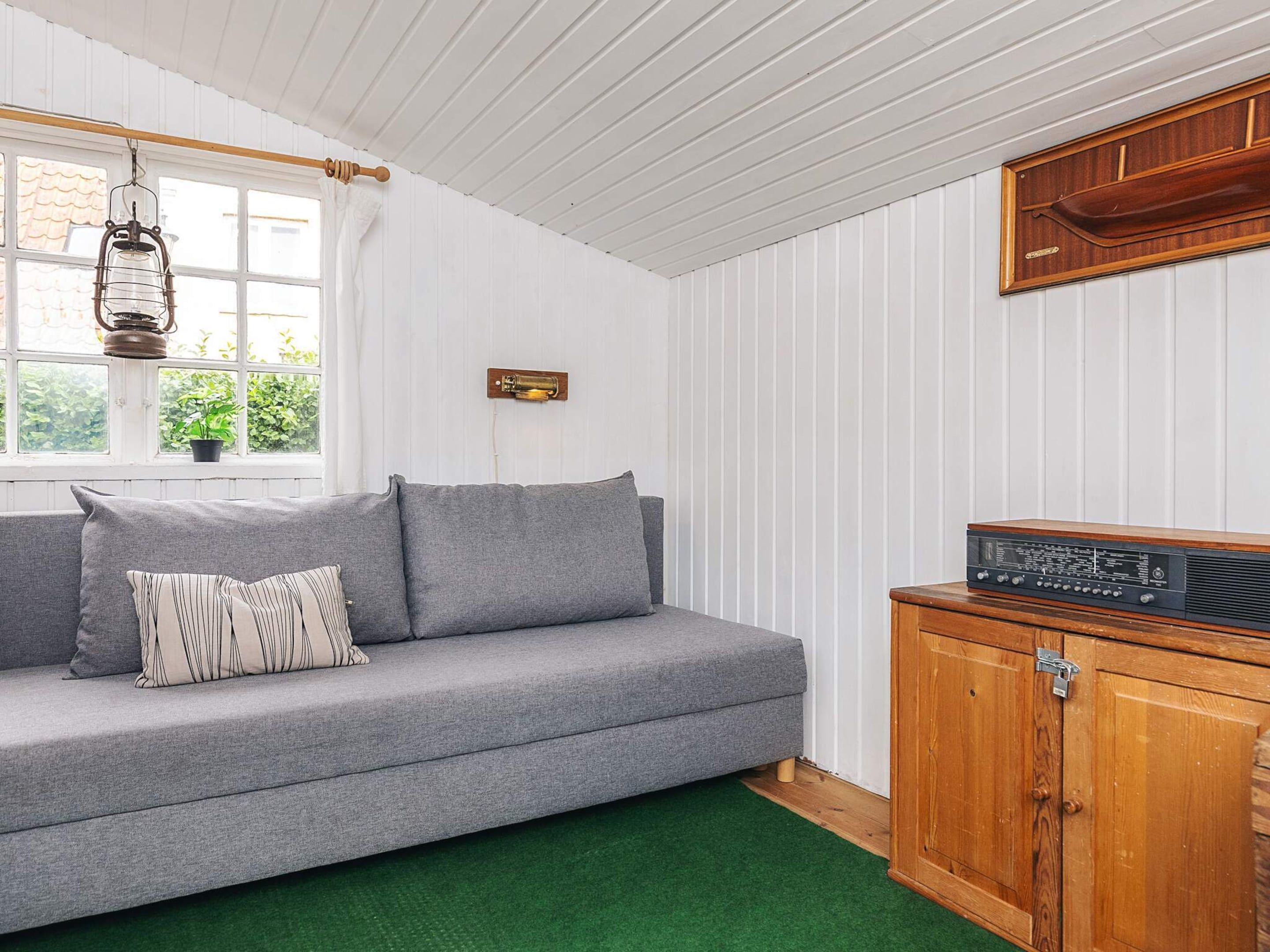 A room with a grey sofa, a wooden cabinet, and a window with a hanging light fixture.