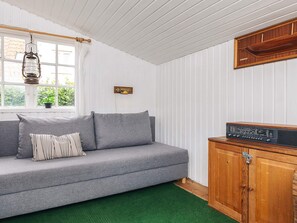 A room with a grey sofa, a wooden cabinet, and a window with a hanging light fixture. - 4 Person Holiday Home in Aeroskobing (Aeroskobing)