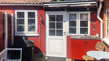 Ein rotes Gebäude mit einer weißen Tür, einem Fenster, einem Waschbecken, einem Tisch mit Stühlen und einem Grill.