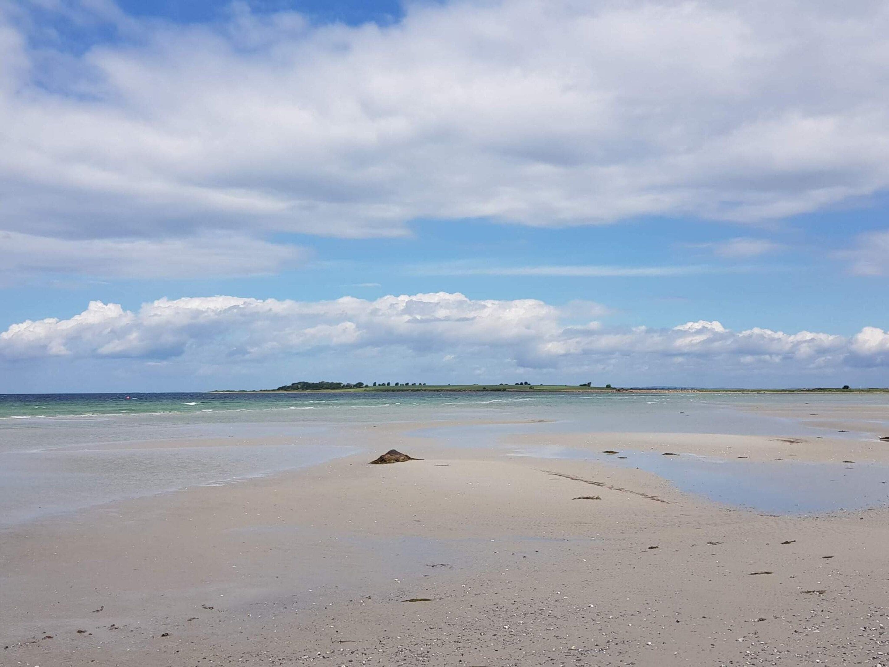 A beach with a sandy shore, calm water, and a distant landmass under a cloudy sky.