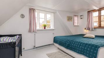 A bedroom with a bed, a radiator, a window with curtains, a small potted plant, and a wall-mounted light.