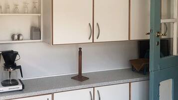 A kitchen with white cabinets, a coffee maker, and a shelf with glassware.