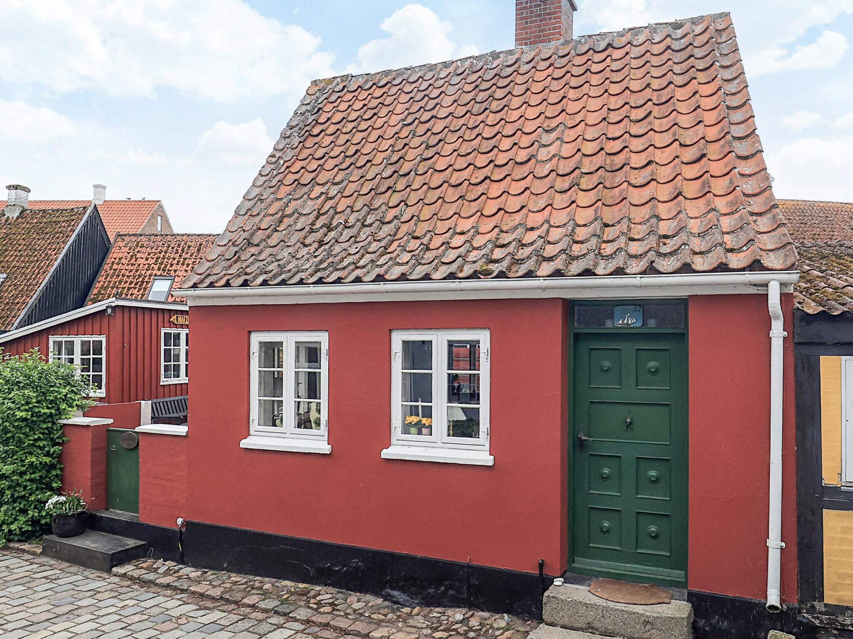 Un bâtiment rouge avec une porte verte, des fenêtres blanches et un toit recouvert de tuiles.