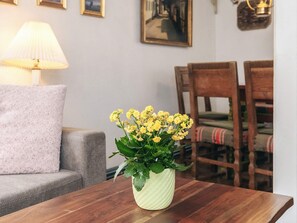 Et værelse med et træbord, en grå sofa, en lampe og en vase med gule blomster.