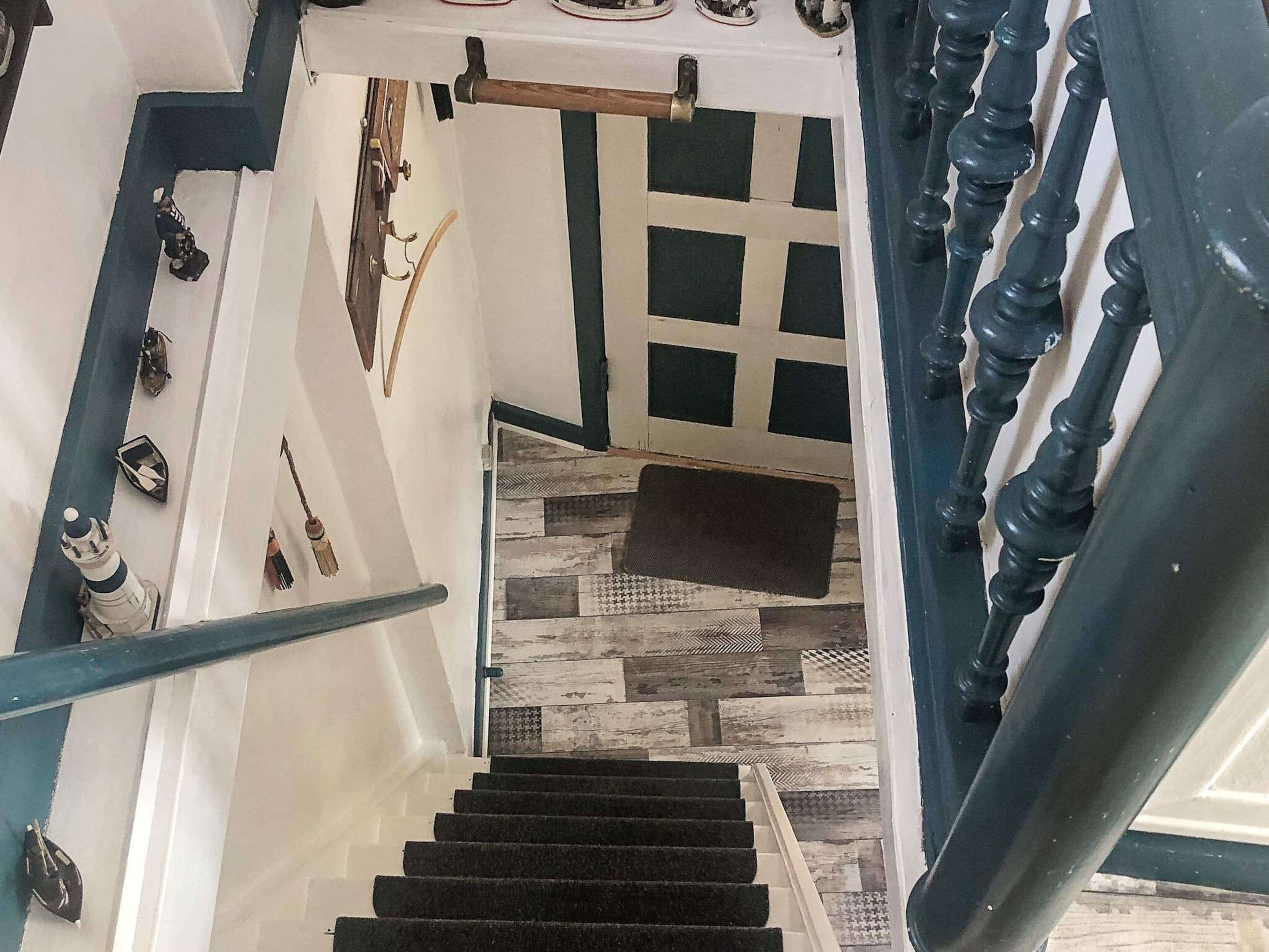 Un escalier dont le sol présente un motif à carreaux, une rampe bleue et une porte ornée d’un motif en réseau.