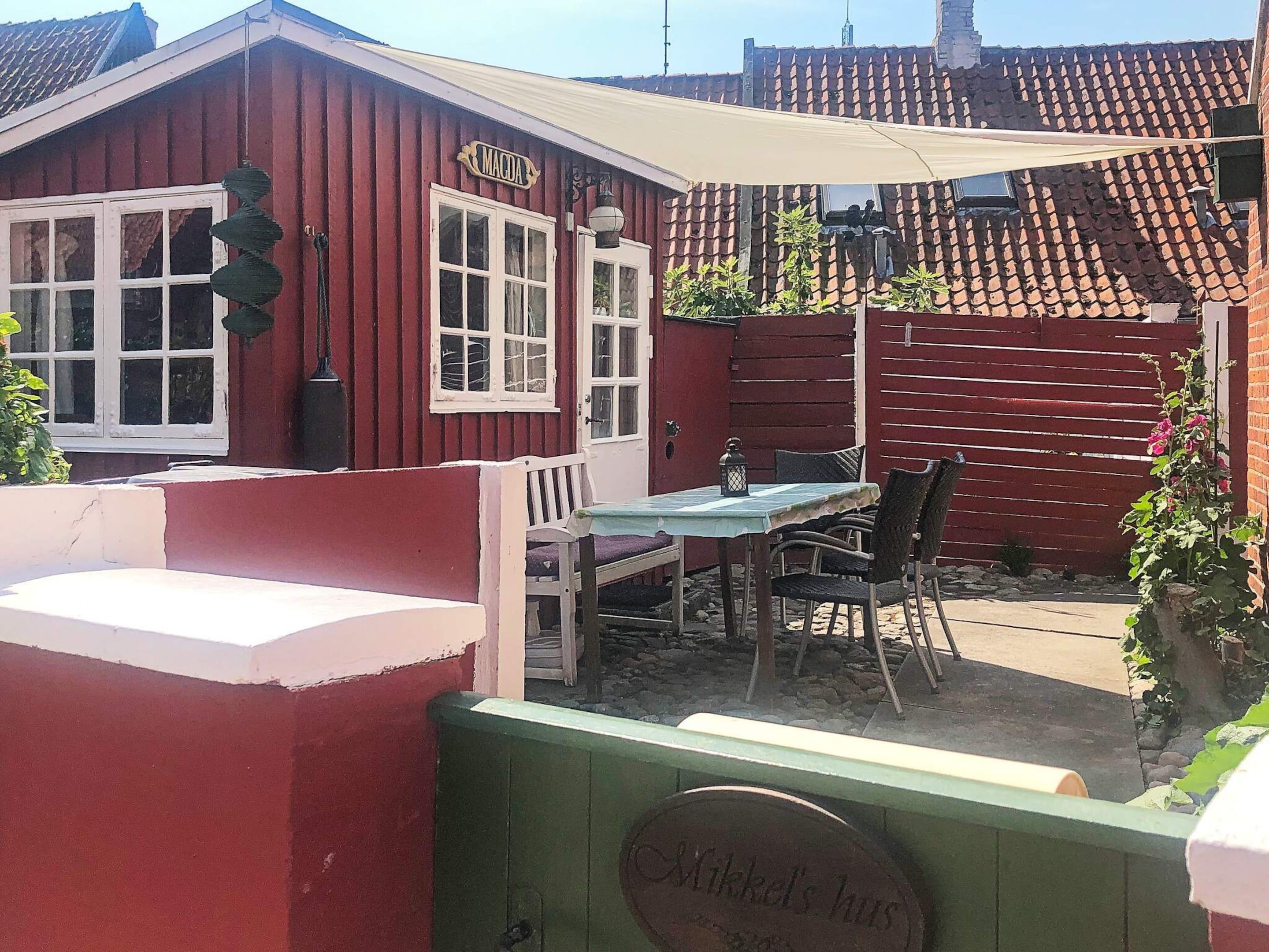 A red wooden building with a sign reading "MACDA" and a table with chairs outside.