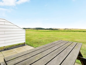 A wooden picnic table in a grassy field with a white building in the background. - Cozy Holiday Home in Jutland near Sea (Lemvig)