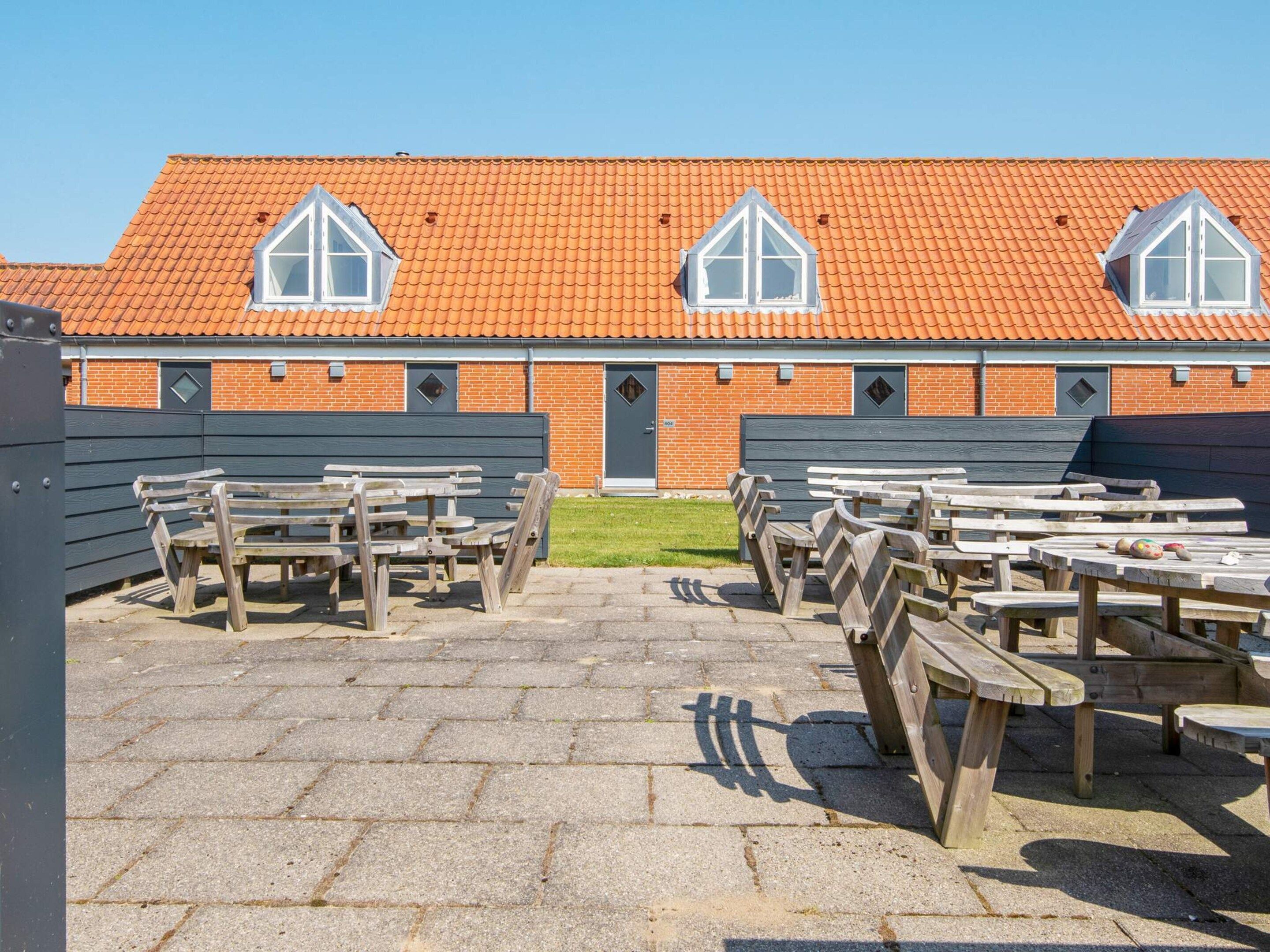 A building with a tiled roof, multiple windows, and a paved area with wooden benches.