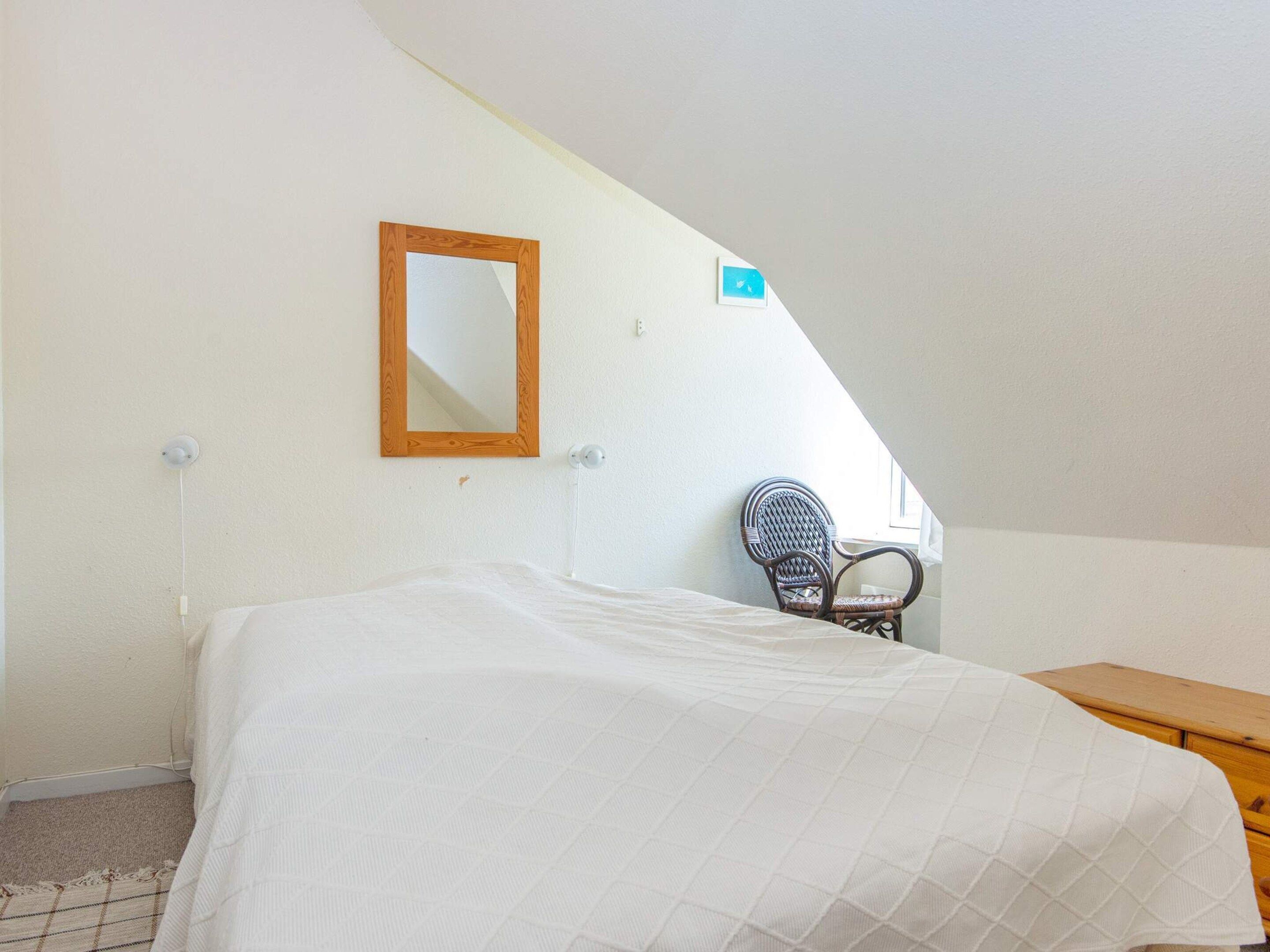 A bedroom with a bed, a chair, a wooden dresser, a mirror, and a small window.