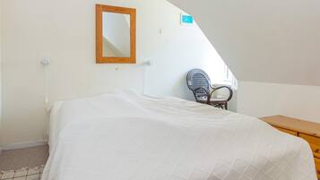A bedroom with a bed, a chair, a wooden dresser, a mirror, and a small window.
