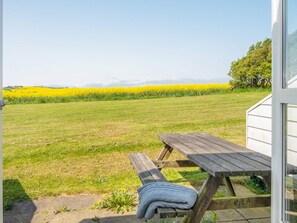 A picnic table with a blanket, a grassy field, and a yellow flower field in the background. - Cozy Holiday Home in Jutland near Sea (Lemvig)