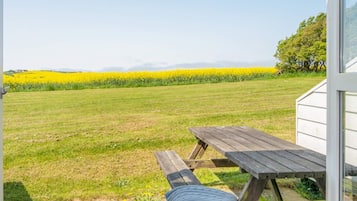 Uma mesa de piquenique com um cobertor, um campo gramado e um campo de flores amarelas ao fundo.