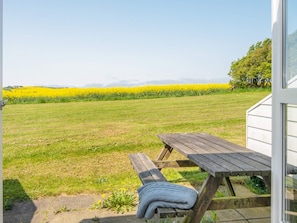 A picnic table with a blanket, a grassy field, and a yellow flower field in the background. - Cozy Holiday Home in Jutland near Sea (Lemvig)