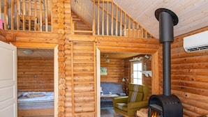 A log cabin interior with a loft bedroom, a sofa, a green armchair, and a wood-burning stove. - 4 Person Holiday Home in Hovborg (Hovborg)