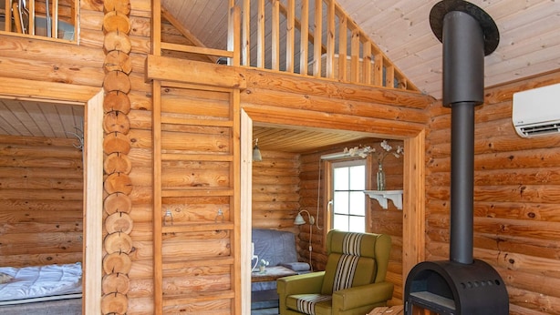 A log cabin interior with a loft bedroom, a green armchair, a fireplace, and a window with a view. - 4 Person Holiday Home in Hovborg-by Traum (Hovborg)