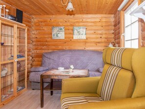 A cozy cabin interior with a wooden log wall, a purple sofa, a yellow armchair, and a small table with a teapot and cup. - 4 Person Holiday Home in Hovborg (Hovborg)