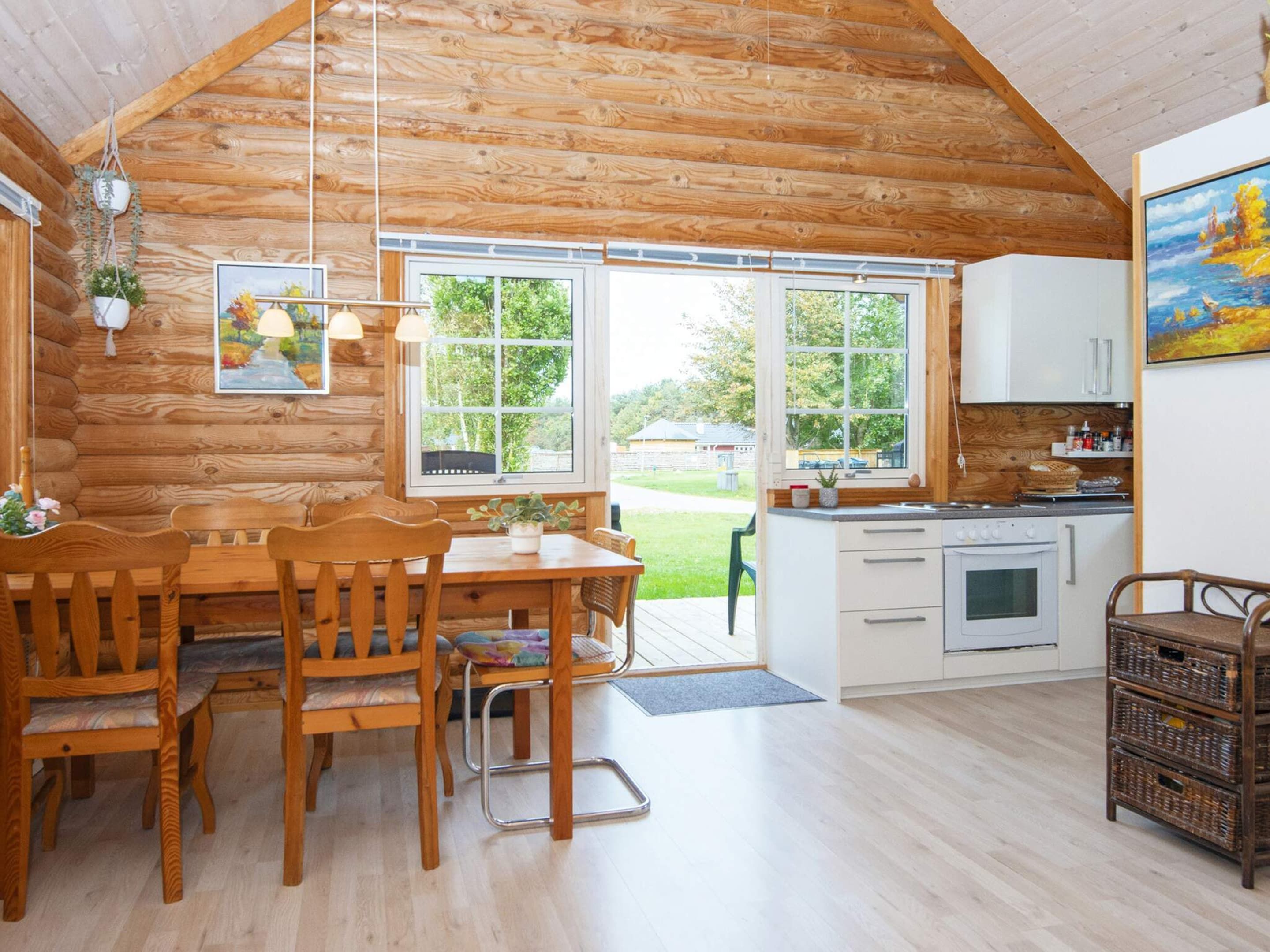 Una cabaña acogedora con interior de madera, comedor, cocina y un ventanal con vistas al exterior.