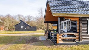 A log cabin with a porch, a separate building in the background, and a grassy area. - 4 Person Holiday Home in Hovborg-by Traum (Hovborg)